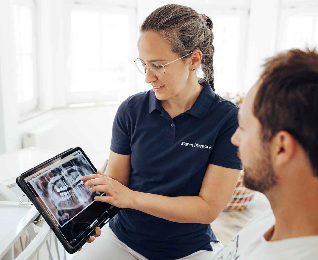 zahnarztpraxis-hlavacek-angstpatienten-vorteile Zahnärztin Maren Hlavacek zeigt einem Patienten sein Röntgenbild auf dem Tablet.