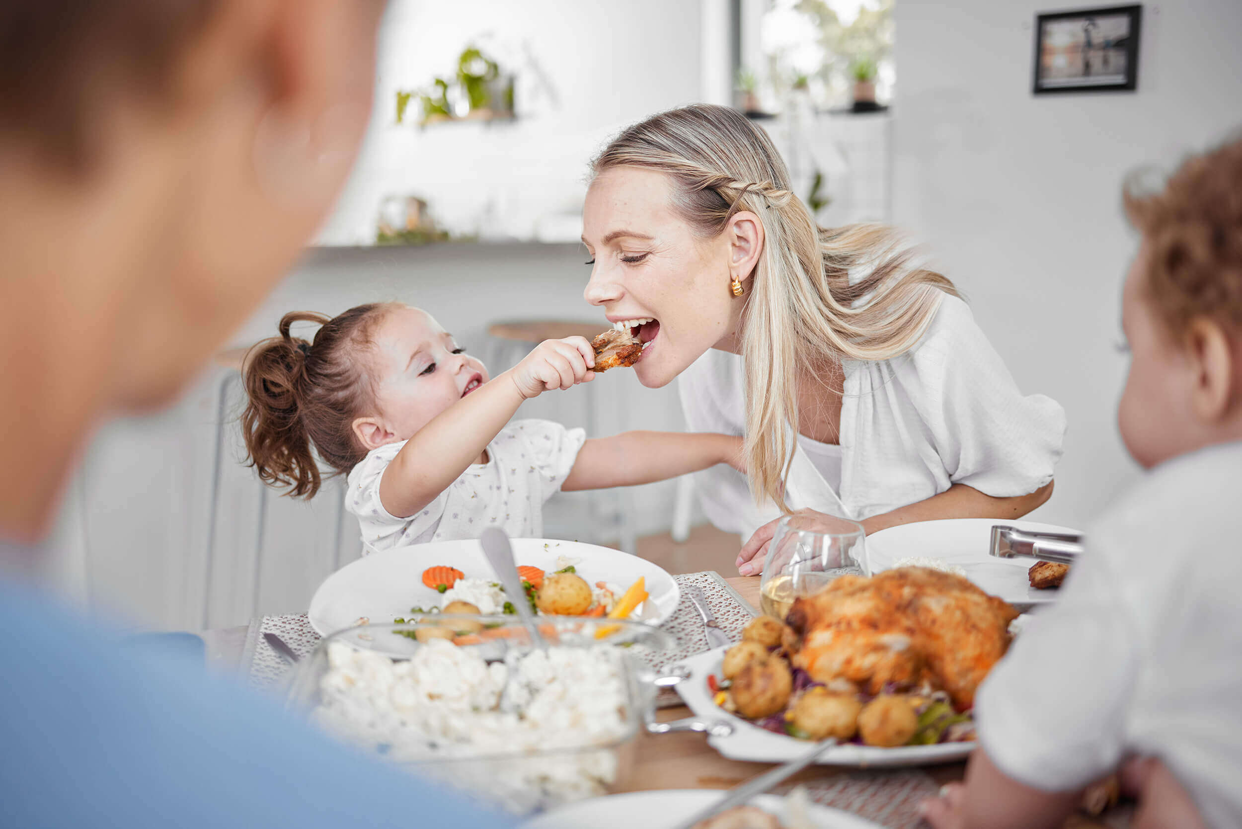 Eine kleine Tochter reicht ihrer mutter eine Hähnchenkeule. Die Mutter beisst herzhaft hinein.